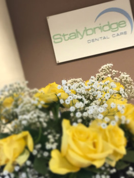 Photograph of bouquet of yellow and white flowers in soft-focus in reception with Stalybridge Dental Care sign behind