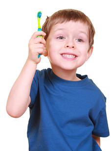 Photograph of young fair-haired boy holding his toothbrush aloft and showing his clean teeth
